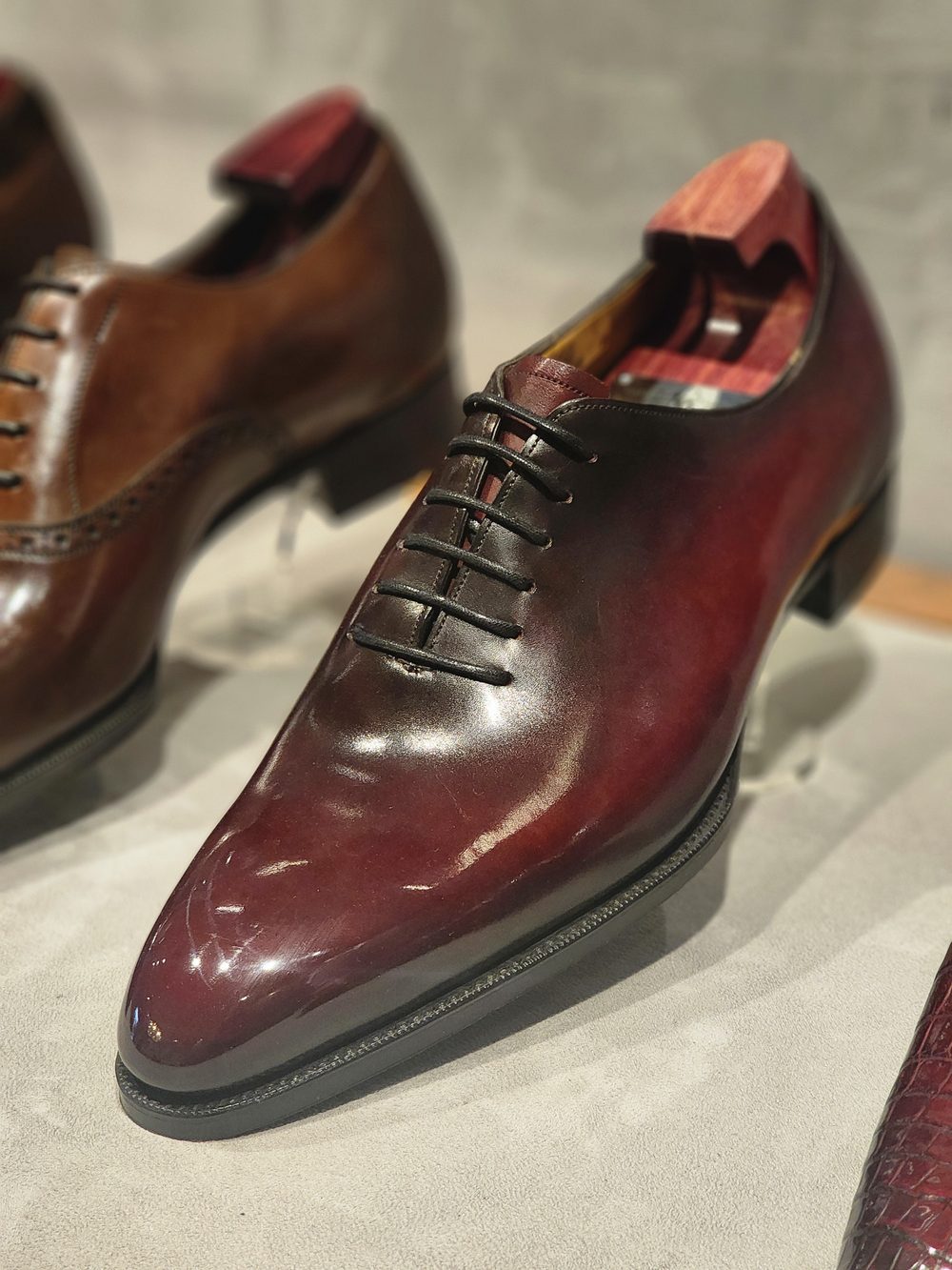A polished burgundy leather dress shoe with a pointed toe and black laces.