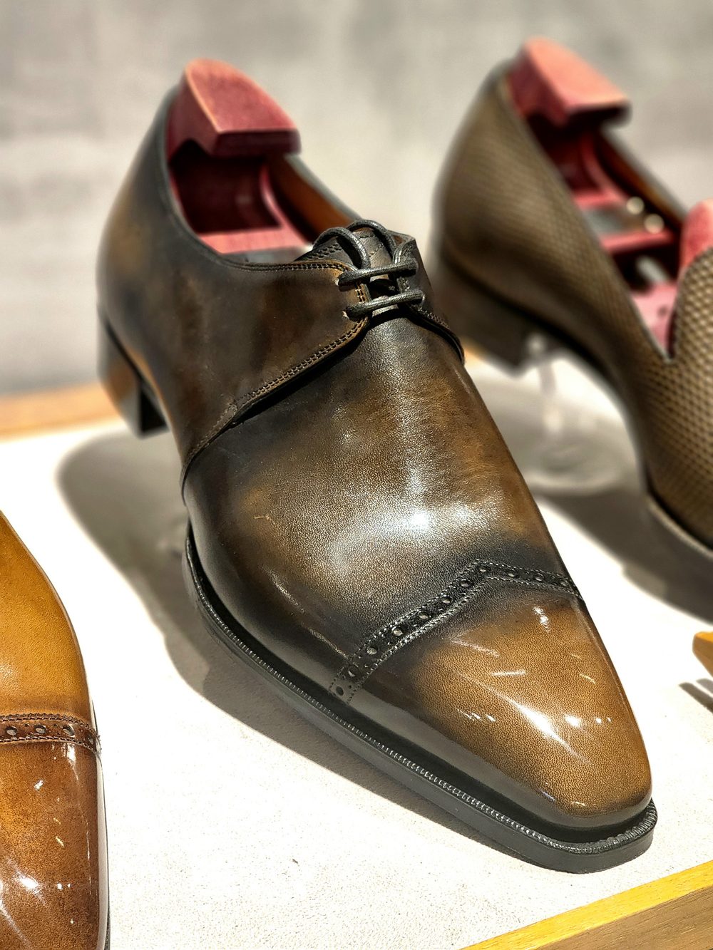 A polished brown leather shoe with a unique toe cap design and decorative stitching.