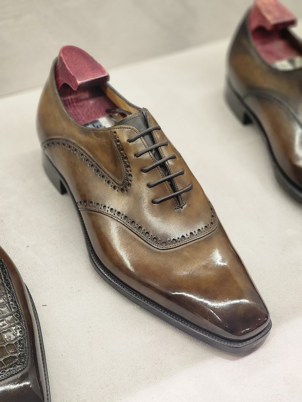 A polished brown leather dress shoe with a pointed toe and decorative broguing along the sides.