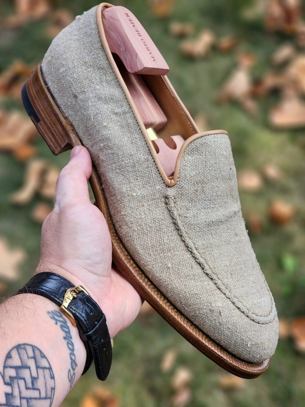 A hand holds a beige Mario Bemer canvas loafer with a wooden shoe tree inside.