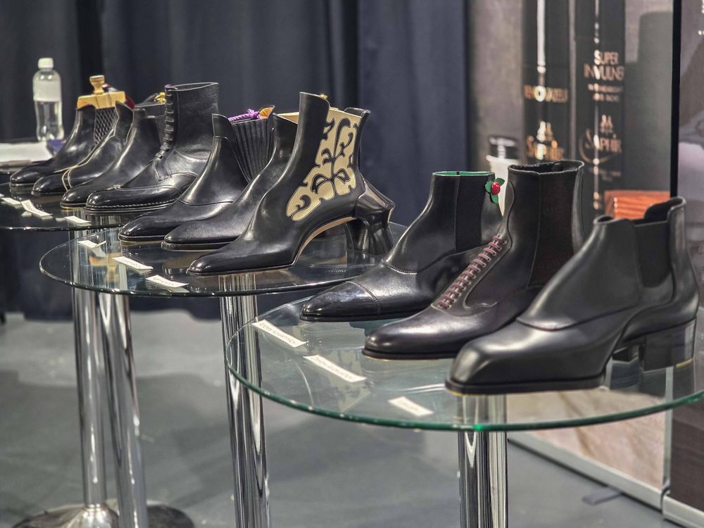 A collection of black leather boots displayed on glass tables, featuring various designs and details.