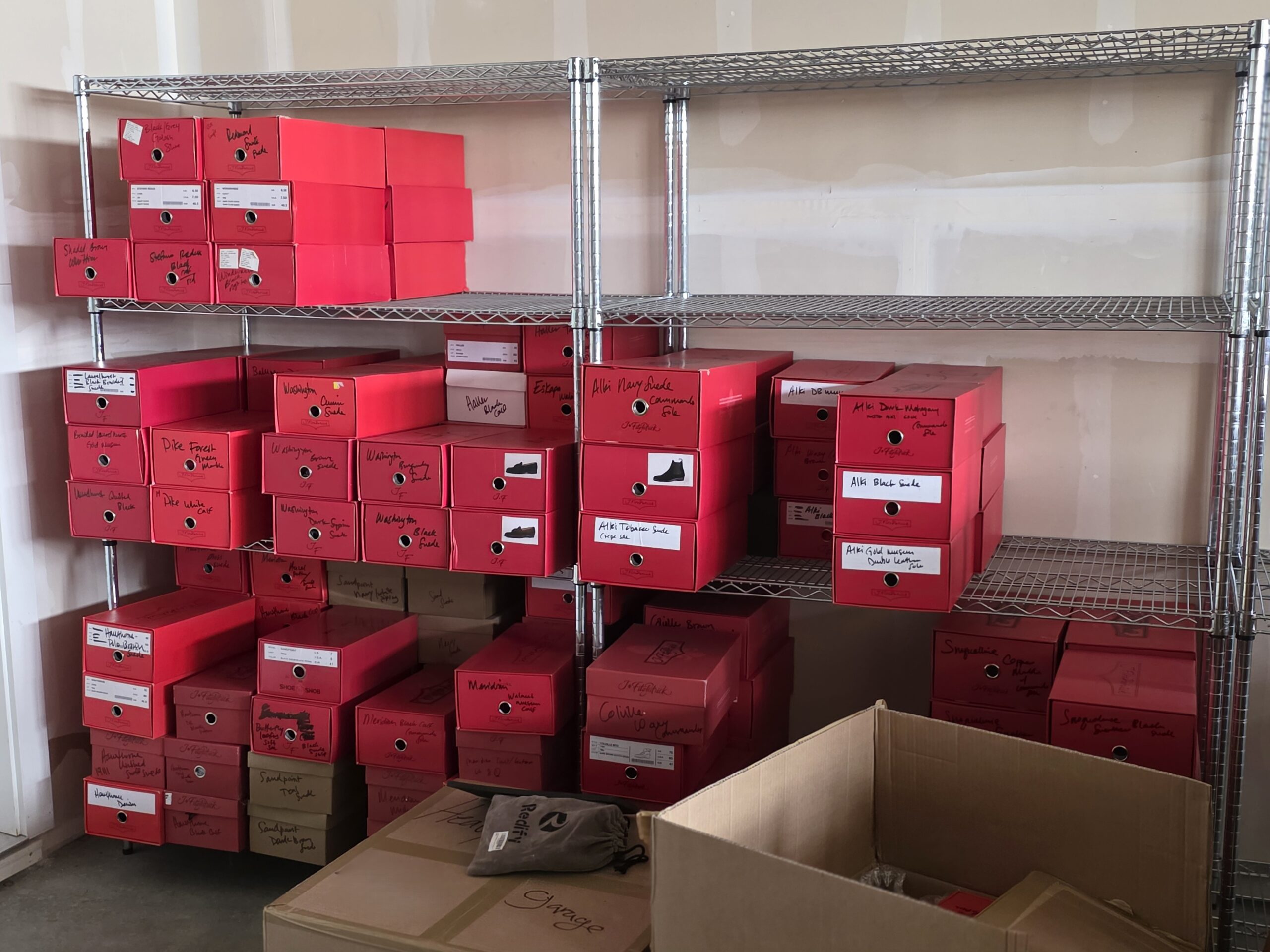 A shelf filled with labeled red boxes, containing various items, with a brown cardboard box in the foreground.