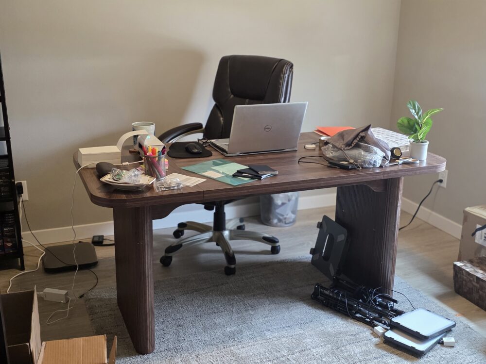 A cluttered wooden desk with a laptop, stationery, a small plant, and various office supplies.