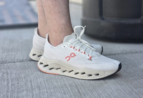 A close-up of a person's foot wearing white sneakers with coral accents and a unique sole design.