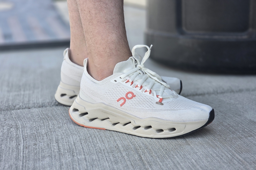A close-up of a person's foot wearing white sneakers with coral accents and a unique sole design.