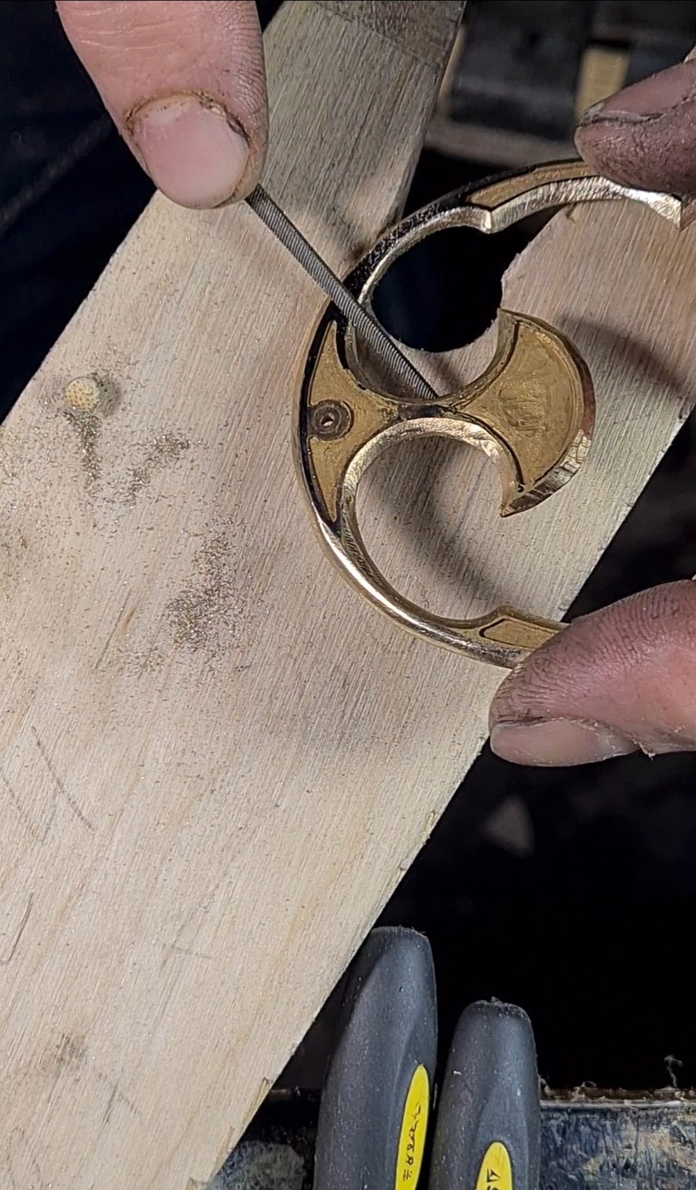 A hand holds a metal shoe component while using a file on it against a wooden surface.