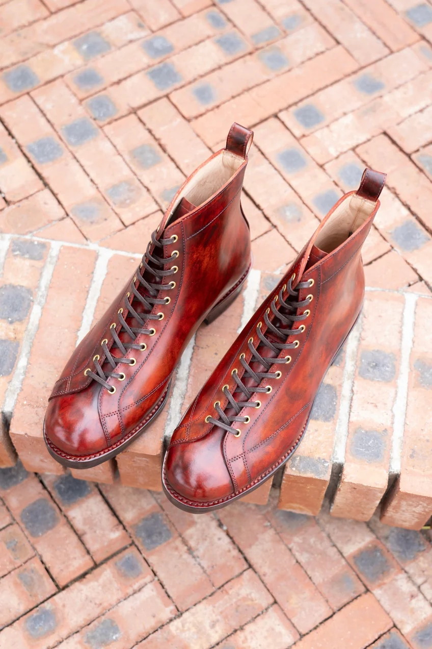 A pair of polished cordovan leather boots in rich brown with gold eyelets and brown laces.