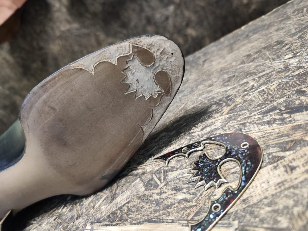 Close-up of a shoe's worn leather sole with decorative cutouts and a shiny, colorful embellishment beside it.