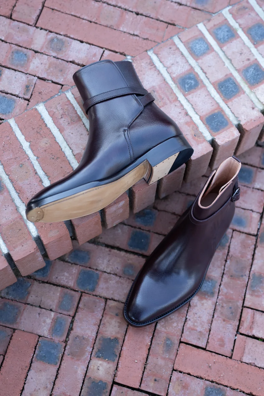 A pair of dark brown cordovan leather ankle boots with a sleek design and wooden soles.
