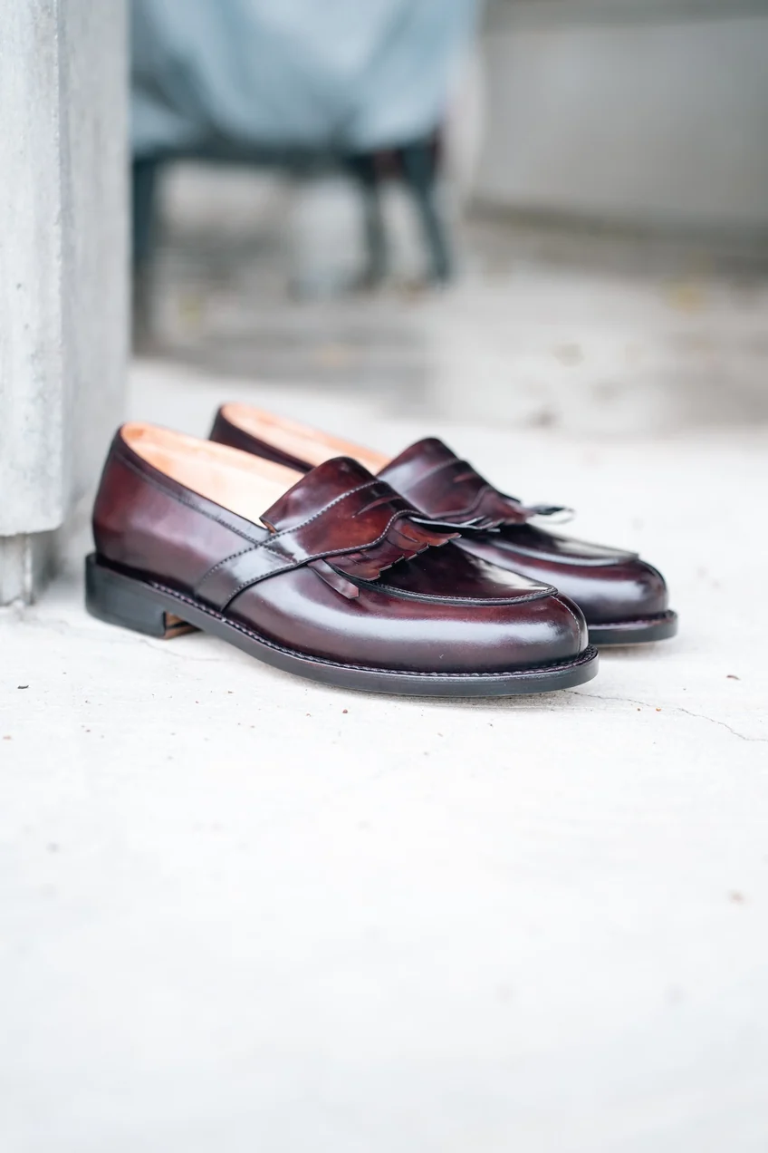 A pair of burgundy leather loafers with a decorative fringe detail.