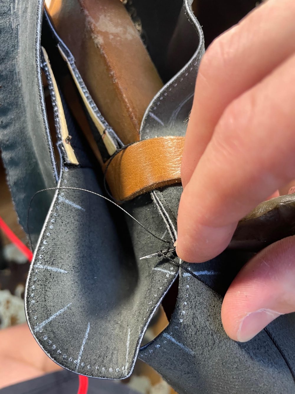 A close-up of a hand sewing black leather pieces together with a needle and black thread.