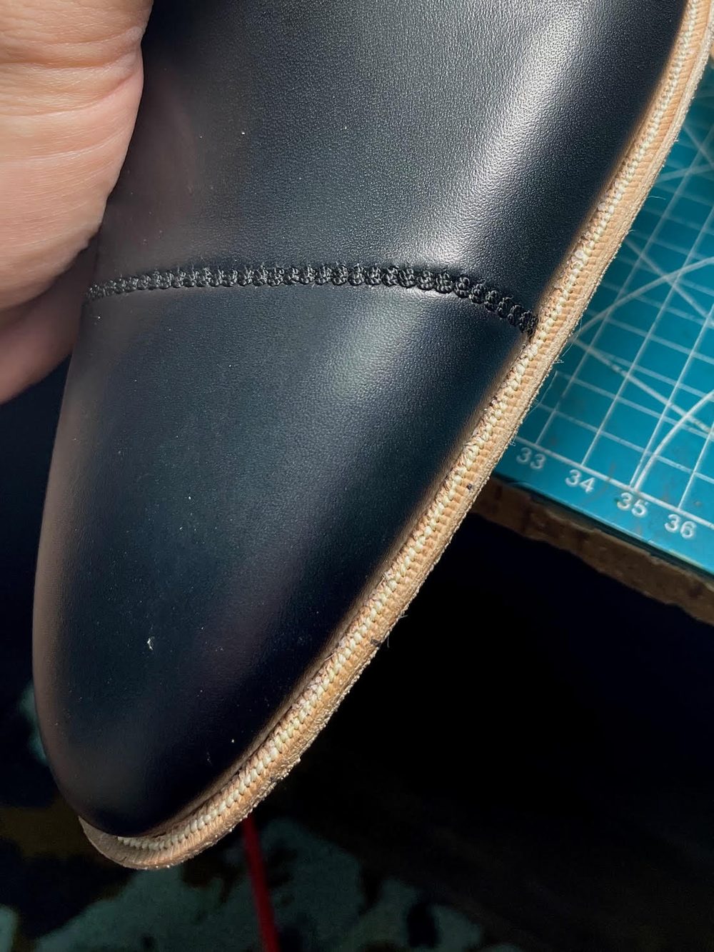 Close-up of a black leather shoe upper with a tan sole and black stitching.
