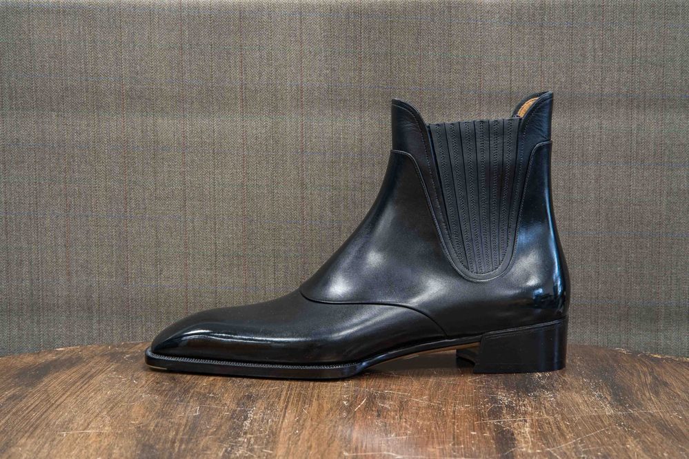 A sleek black leather ankle boot with a structured design and ribbed detailing on the sides.