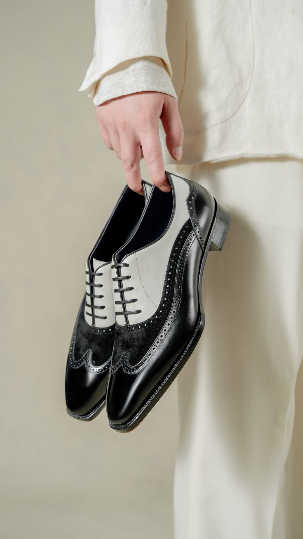 A person holds a pair of black and gray leather dress shoes with decorative perforations.