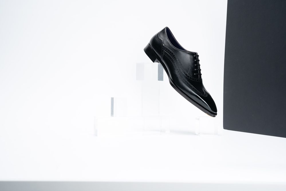 A black leather spectator shoe is floating above clear acrylic stands.