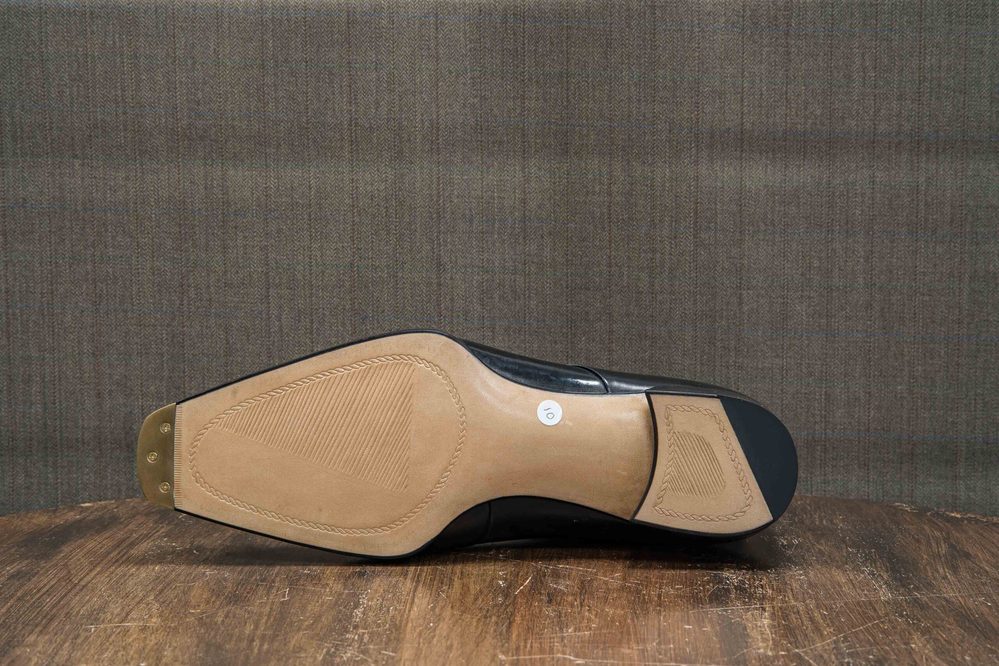 The image shows the sole of a black leather shoe with a tan rubber bottom and a decorative pattern.