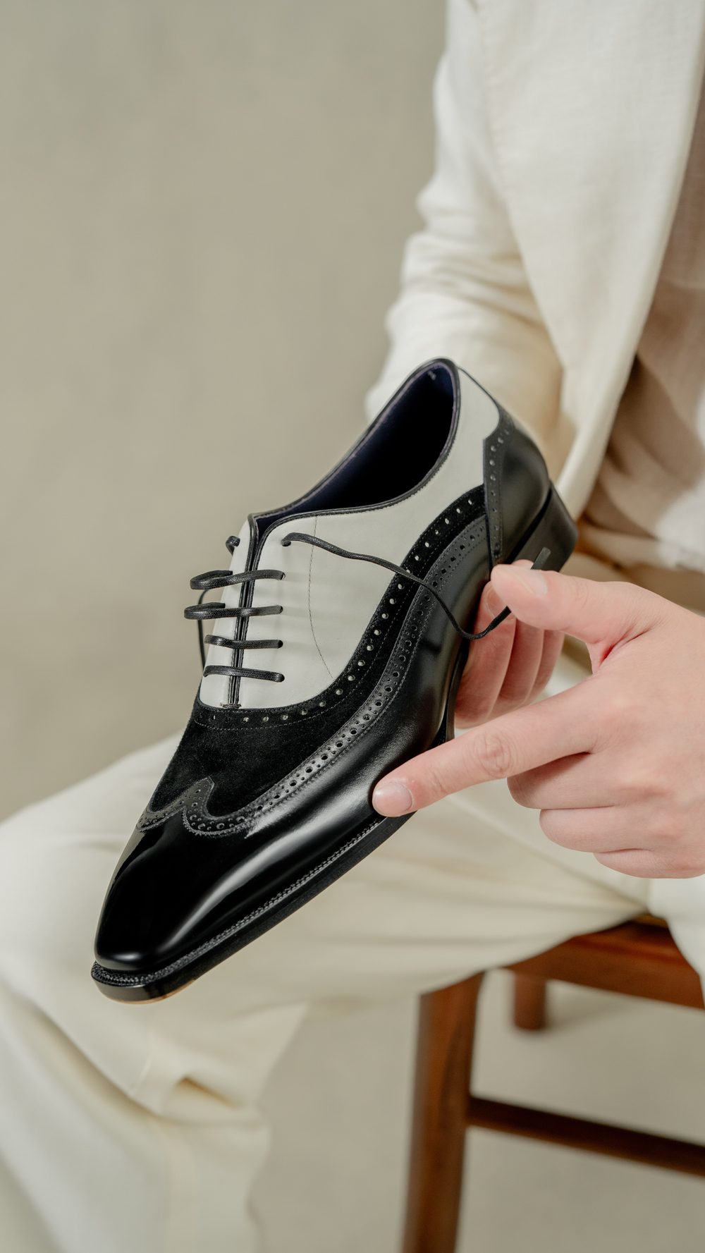 A person holds a black and gray leather dress shoe with intricate detailing and laces.