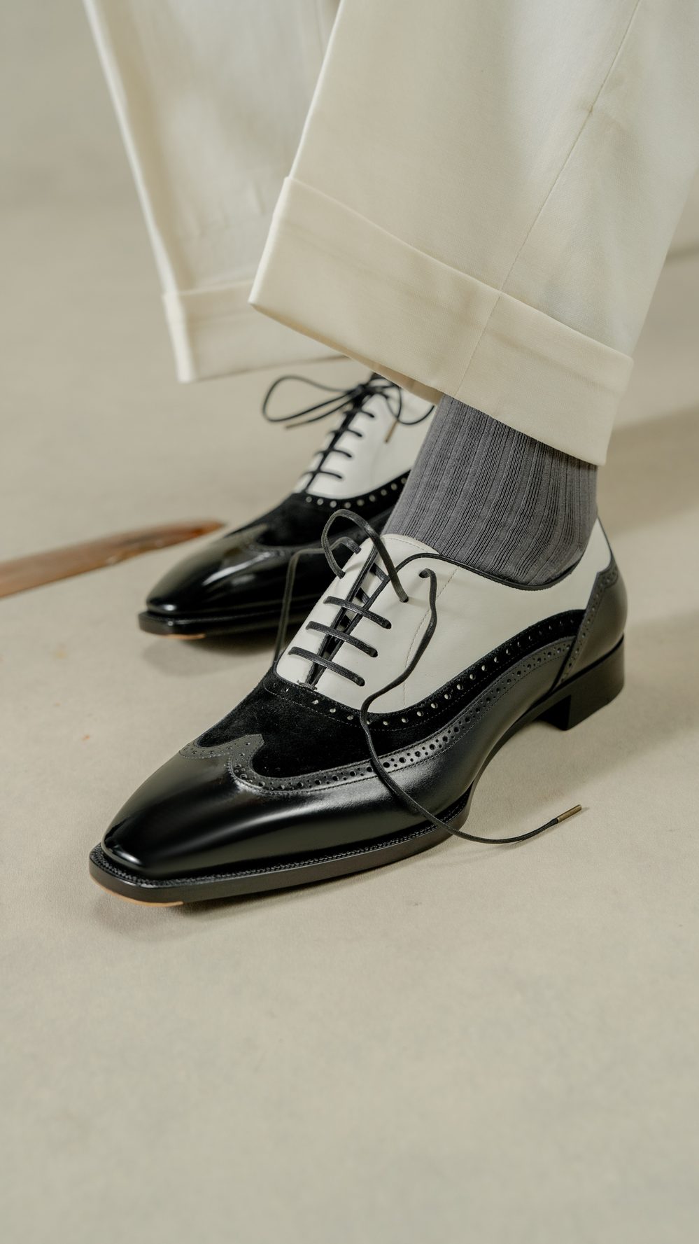 A close-up of black and white spectator shoes with laces and a textured grey sock.