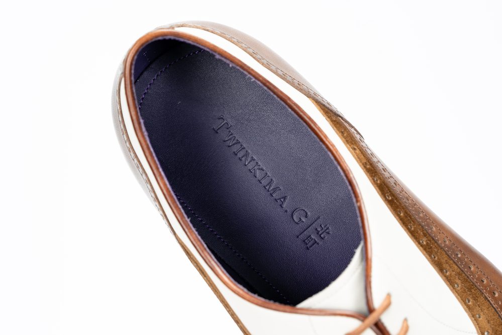 A close-up of a brown and white shoe interior featuring the embossed text "TWINKIMA.G" on a dark purple insole.