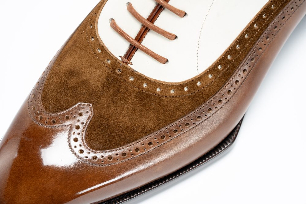 Close-up of a brown leather and suede spectator shoe with decorative perforations and laces.