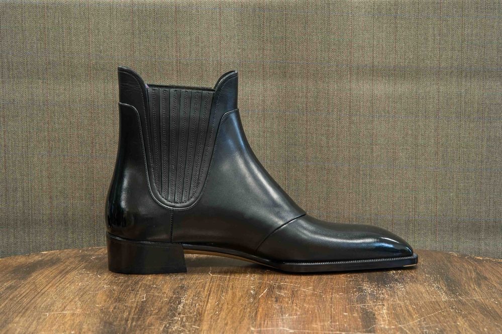 A black leather ankle boot with a sleek design and textured side panels.