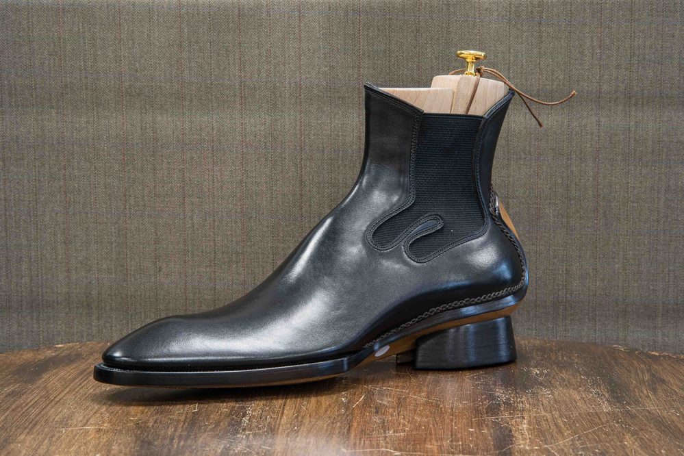 A polished black leather boot with elastic sides and a wooden shoe tree inserted.