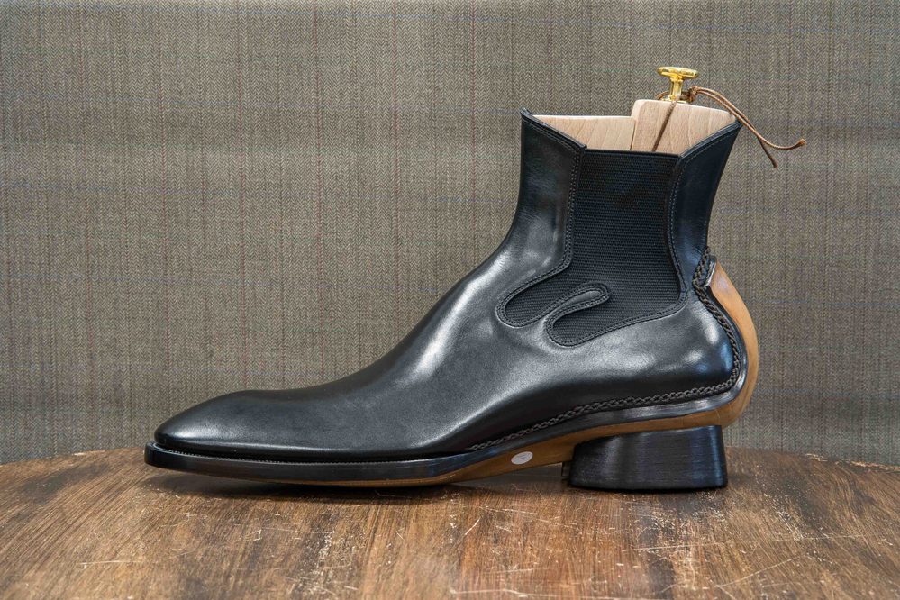 A sleek black leather ankle boot with a wooden heel and elastic side panels.