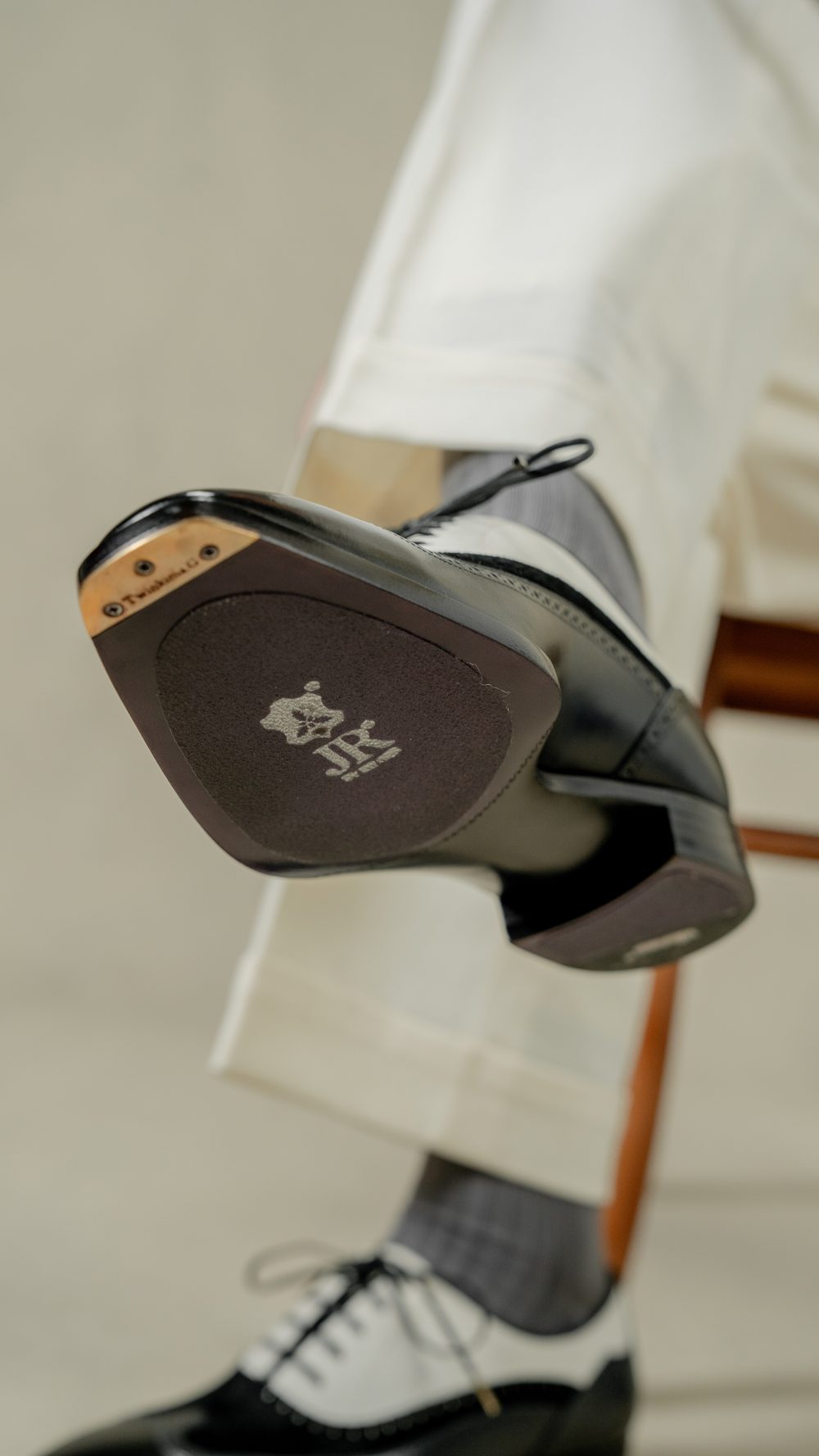 A close-up of a black and white spectator shoe, featuring a prominent logo on the sole.