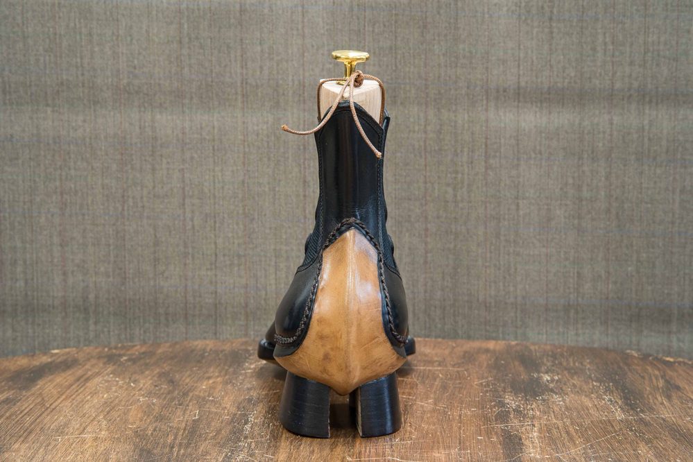 A black and tan leather shoe with a wooden shoehorn and laces, displayed upright on a wooden surface.