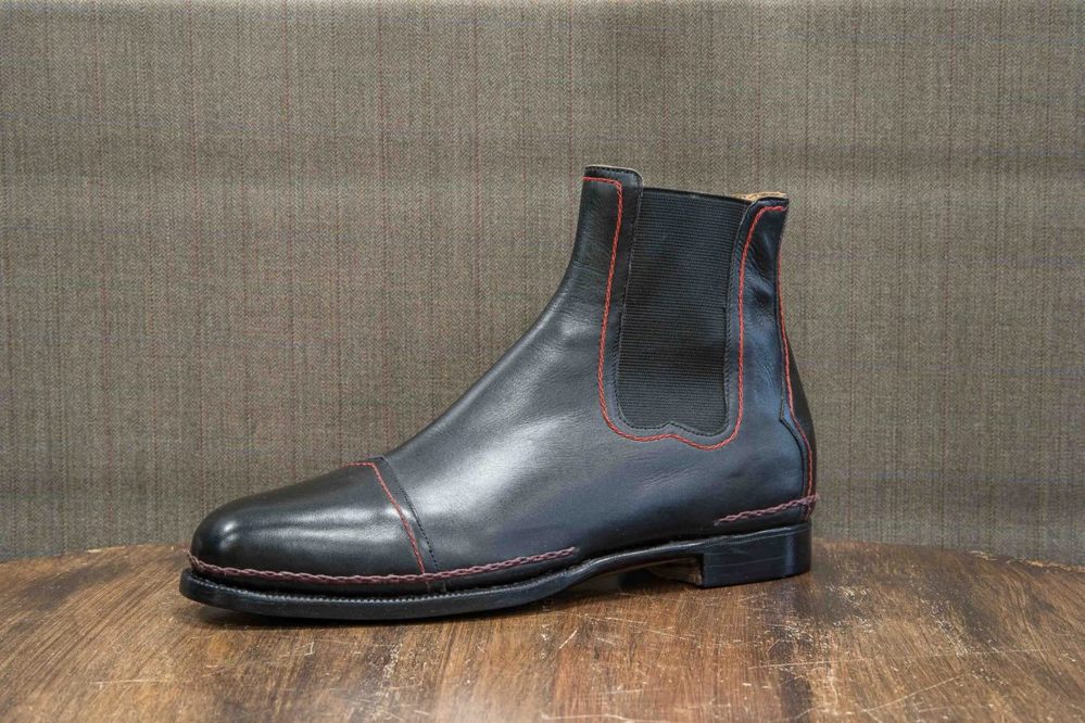 A black leather Chelsea boot with red stitching details.