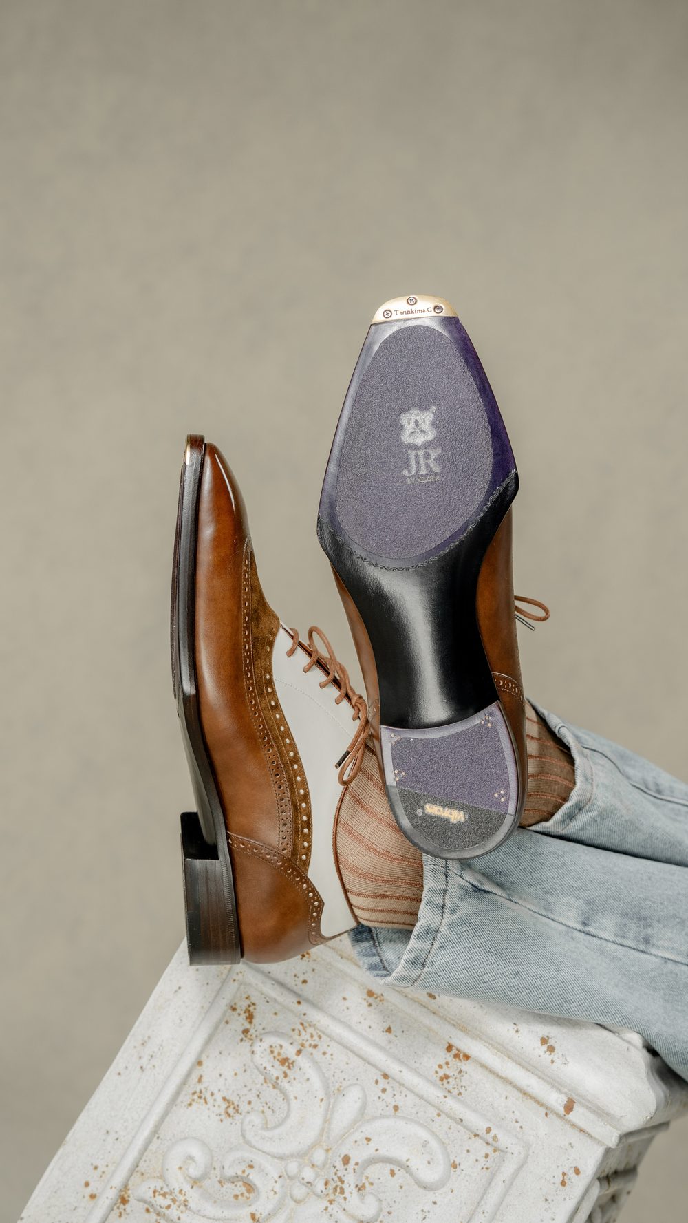 A pair of brown and white spectator shoes with detailed stitching and a black sole, showcasing the shoe's underside.
