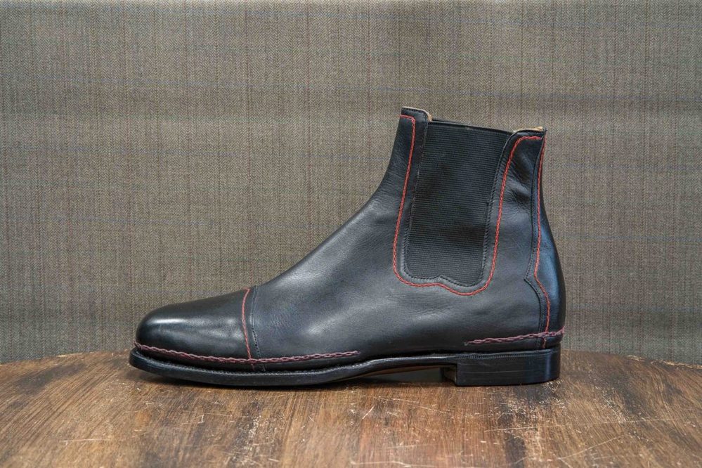 A black leather ankle boot with red stitching.