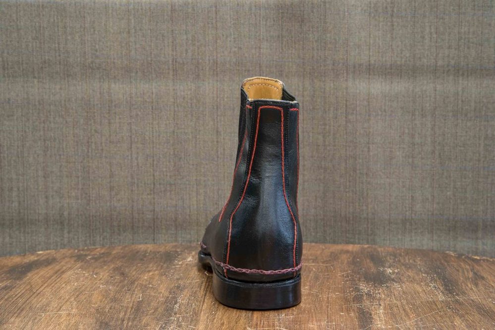 A black leather boot with red stitching, viewed from the back.