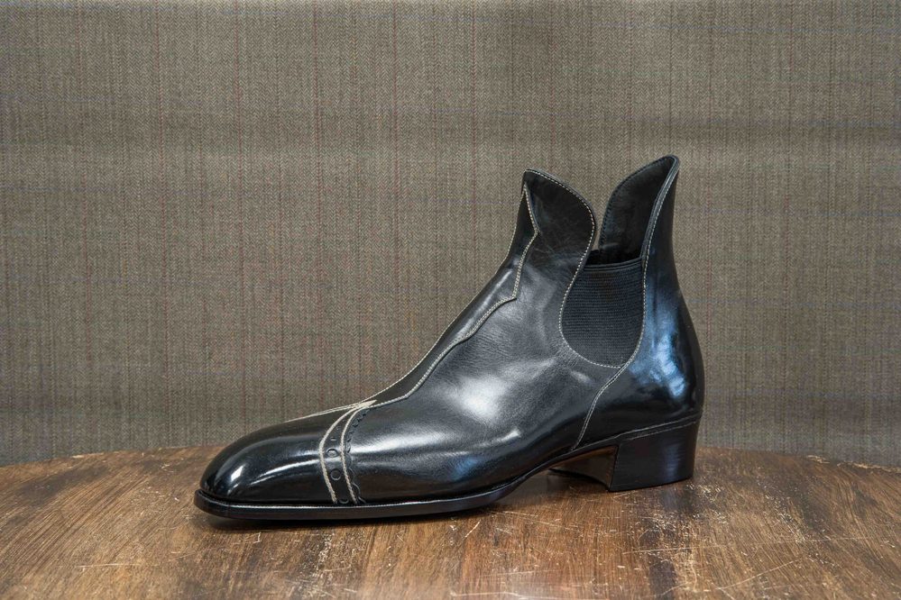A sleek black leather boot with a low heel and elastic side panels.