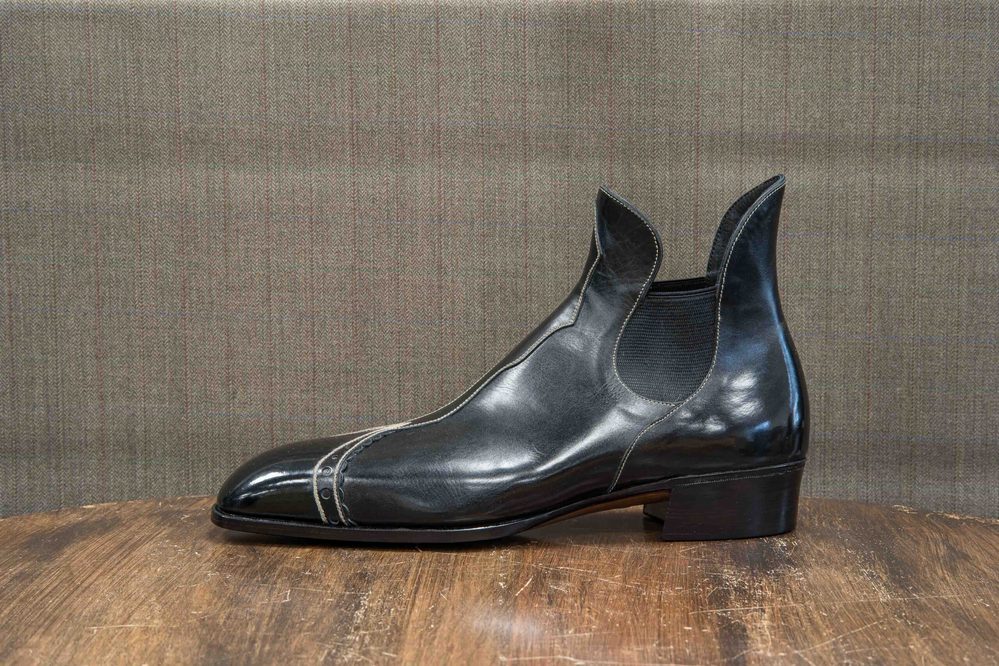 A sleek black leather boot with elastic side panels and decorative stitching.