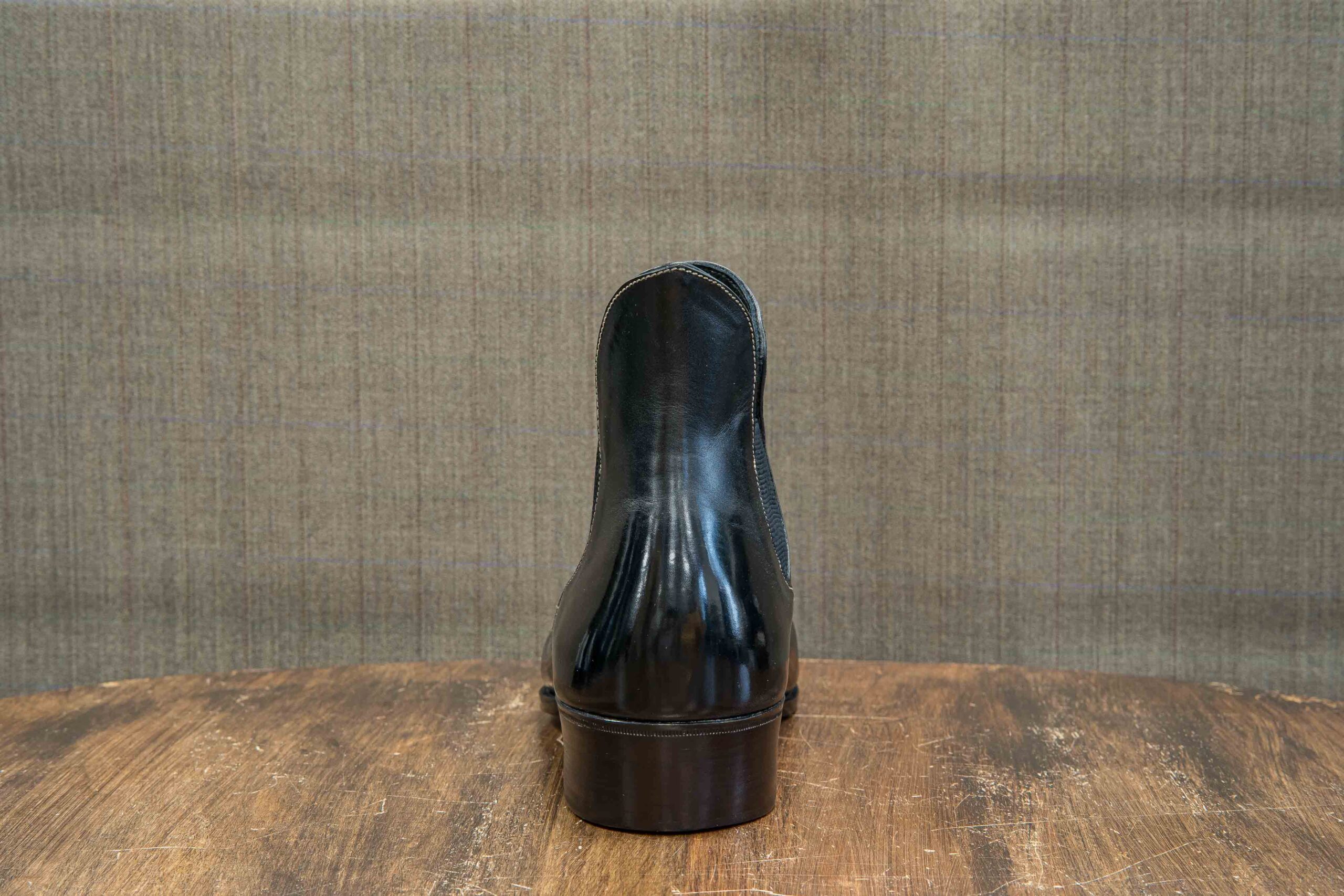 A polished black leather shoe viewed from the back, showcasing its sleek design and curved heel.