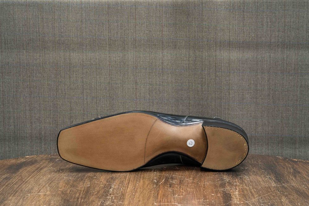 The image shows the sole of a polished black shoe with a tan leather outsole.