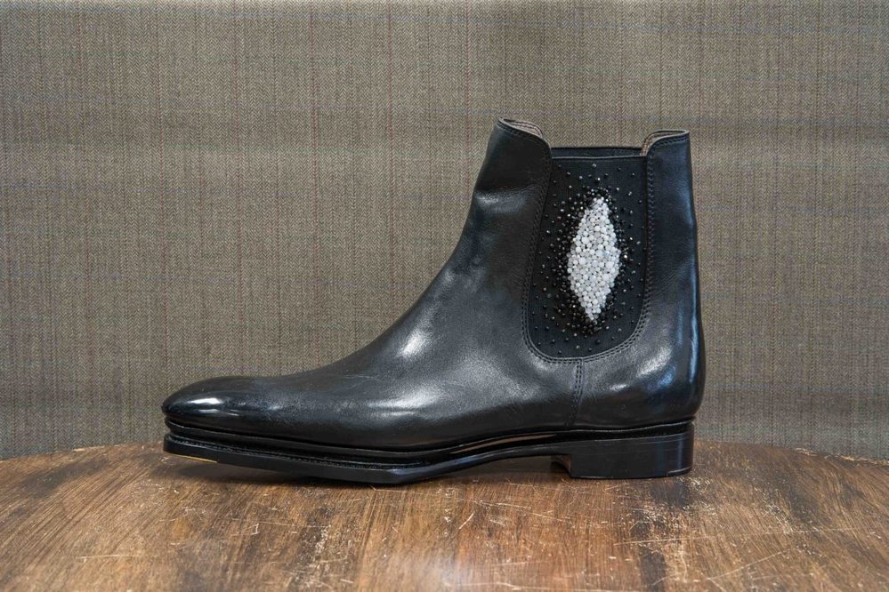 A black leather ankle boot with decorative beadwork in a diamond shape on the side.