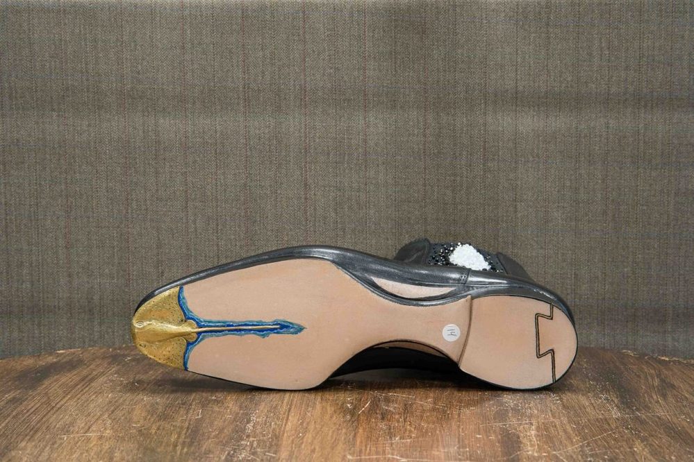 A black shoe sole with a gold and blue design, featuring a smooth beige surface.