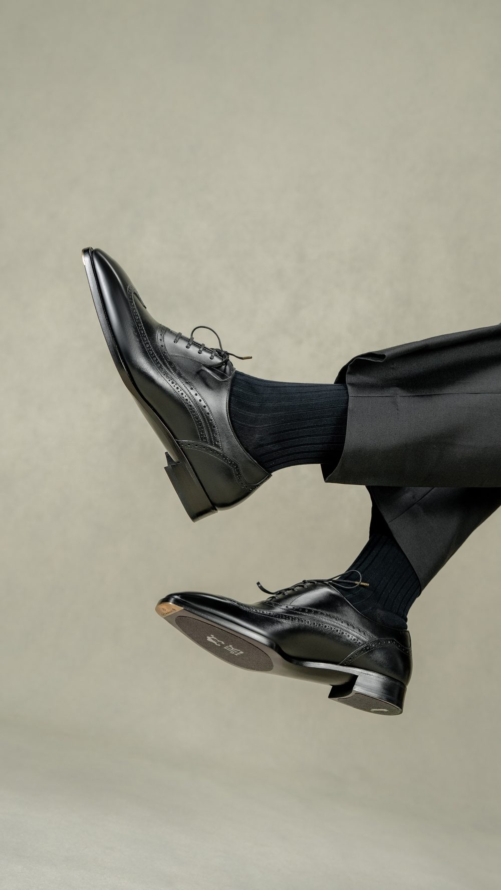 A close-up of polished black leather spectator shoes paired with black ribbed socks.