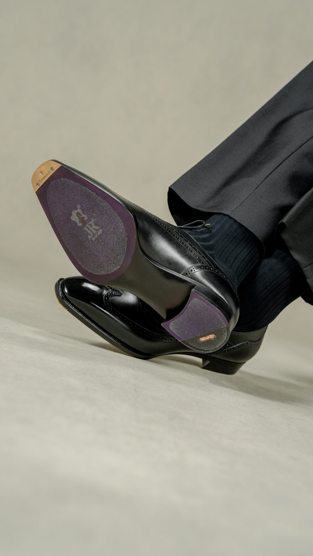 A close-up of a polished black dress shoe with a purple sole, partially visible above dark dress pants.
