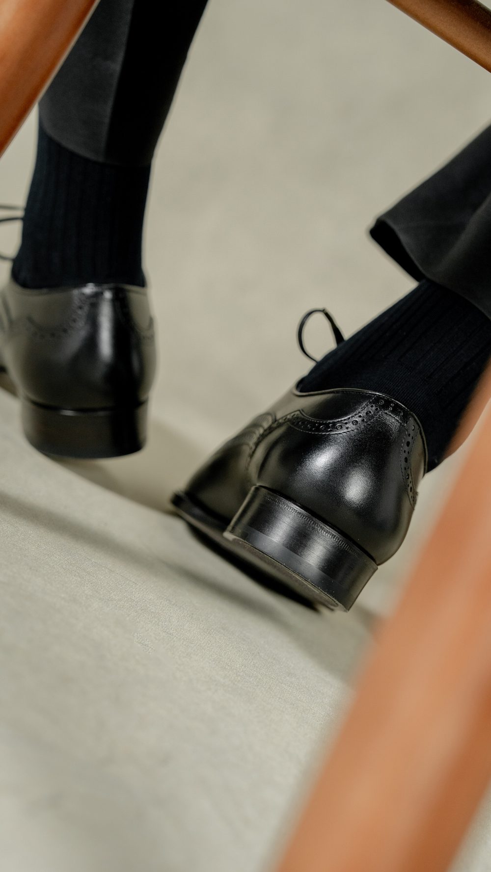 Black leather dress shoes paired with ribbed black socks are positioned beneath a chair.