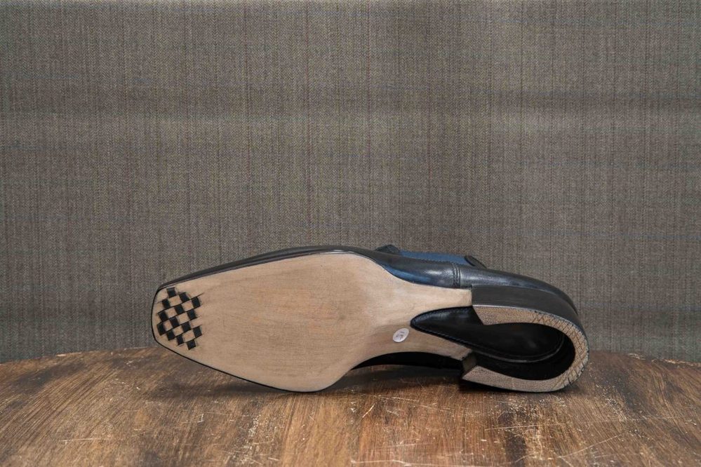 A black leather shoe with a smooth sole and a checkered pattern on the heel, viewed from underneath.