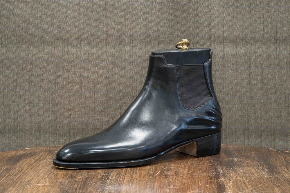 A polished black leather ankle boot with a gold-colored pull tab.