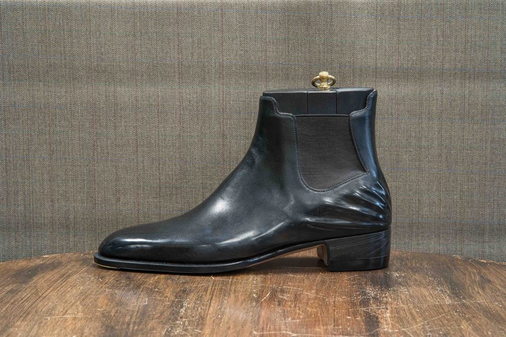 A sleek black leather boot with a low heel and elastic side panels.