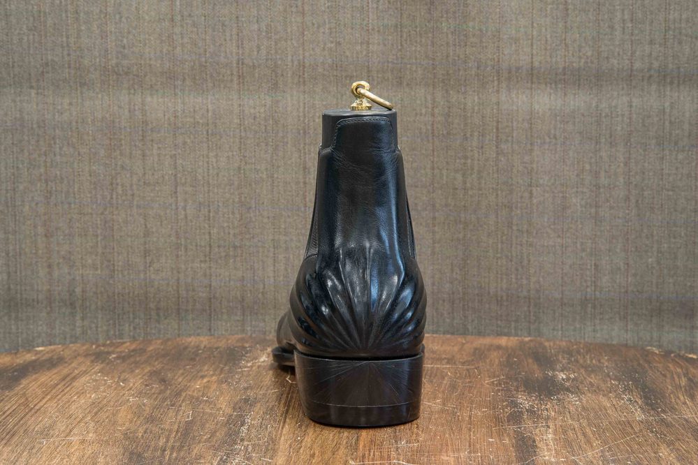 A black leather boot with a decorative scalloped design at the heel.