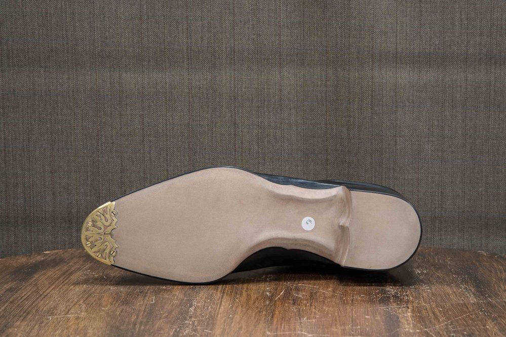 The image shows the sole of a shoe with a smooth beige surface and a decorative gold detail at the toe.