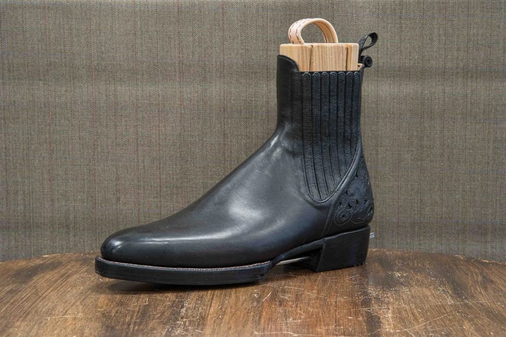 A black leather ankle boot with a textured side and wooden shoehorn.