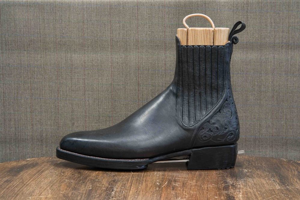 A black leather boot with a ribbed upper and decorative detailing on the side.