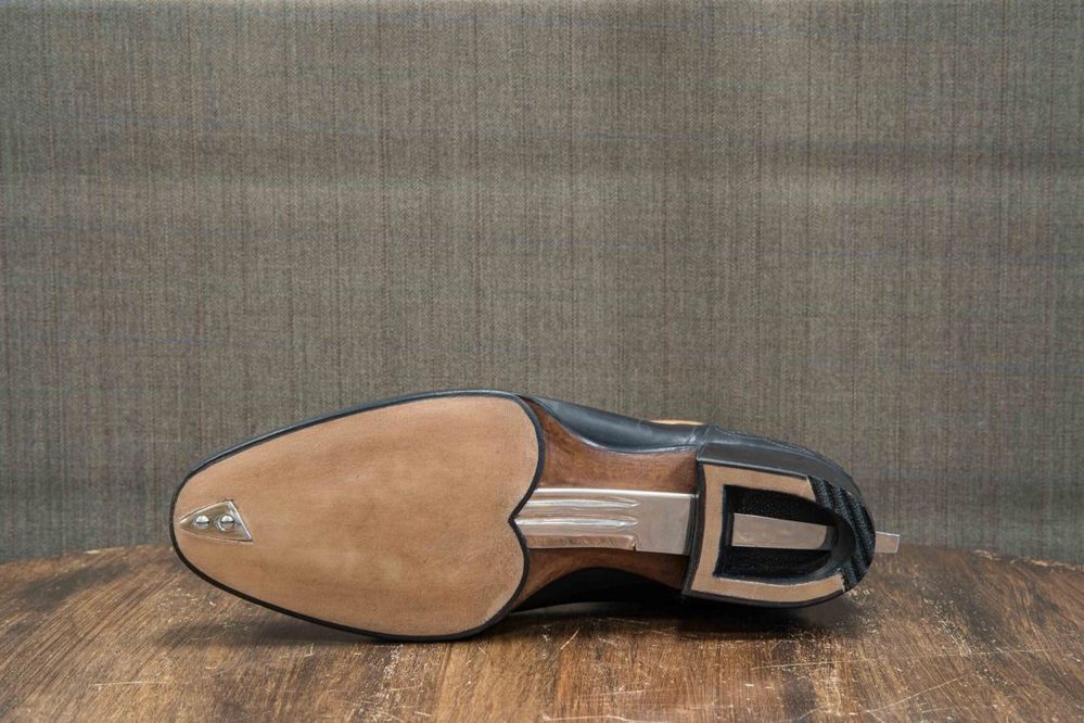 The image shows the sole of a black leather shoe with a beige leather and silver metal accent.